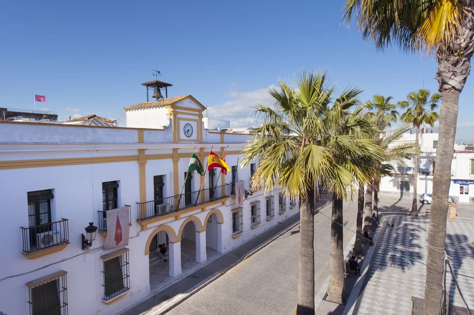 Fachada del Ayuntamiento de Trebujena junto a una plaza con palmeras.